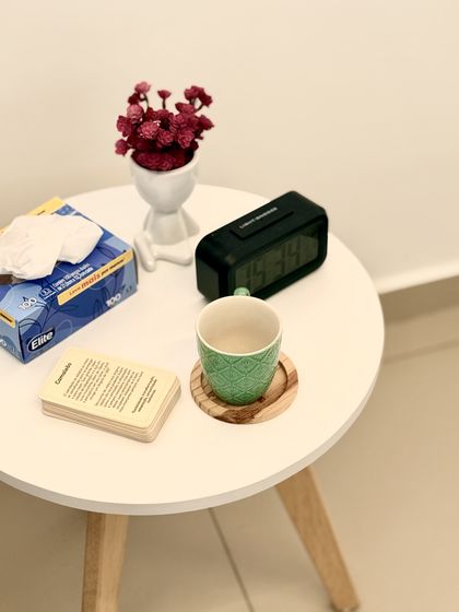 Mesinha de apoio com flores, relógio, lenços e uma xícara verde.