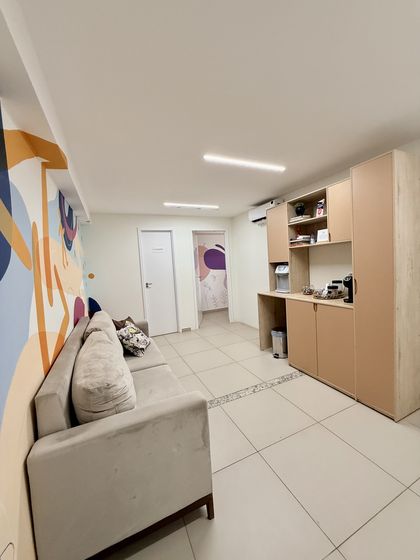 Área de espera com sofá bege, mural colorido na parede e copa ao fundo.